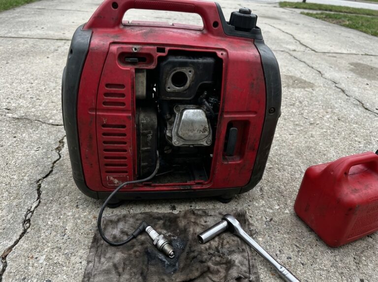 Portable inverter generator on a driveway with its spark plug removed and lying on a rag next to a plug socket wrench and a fuel can